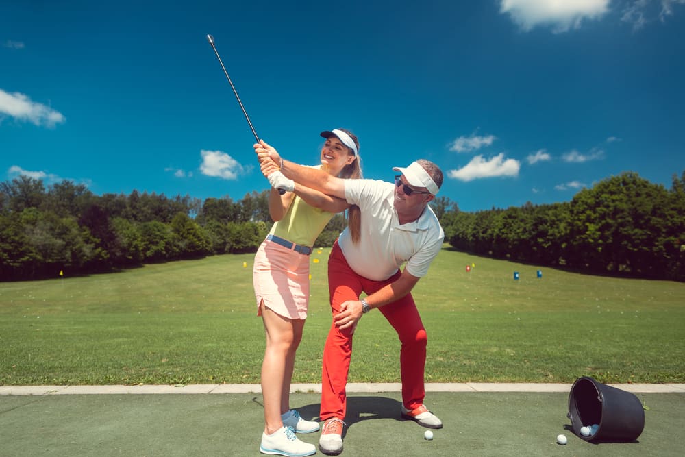 Golf instructor helping female student with swing technique at a professional outdoor driving range in Beachwood, Ohio.
