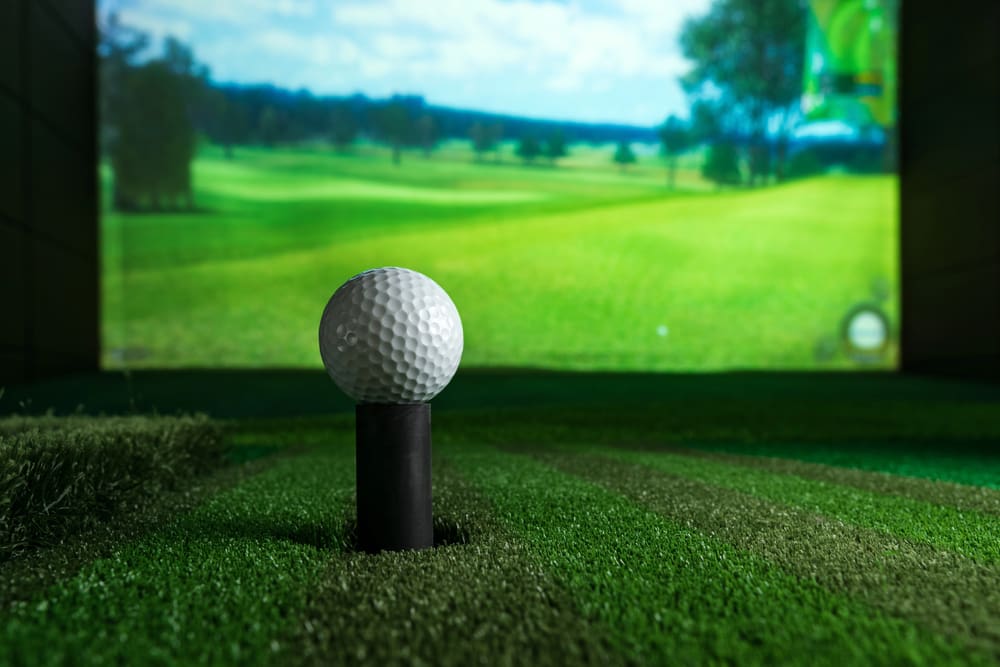Train Year-Round with TrackMan4 Indoor Golf Simulator Golf ball on tee inside indoor simulator with projected golf course in background
